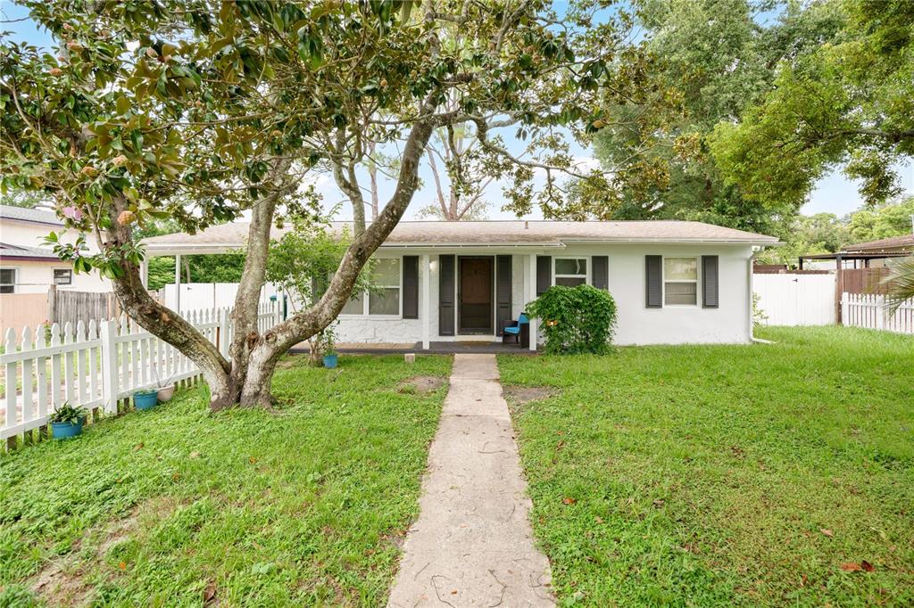 A white single-story house sits behind a white picket fence under a large tree — 682 MERRIMAC STREET, DELTONA, FL