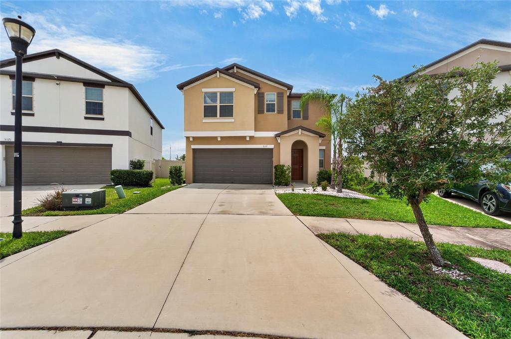 A two-story suburban house with a tan stucco exterior and a two-car garage — 5119 WHITE CHICORY DRIVE, APOLLO BEACH, FL
