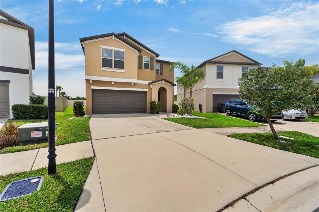 A two-story suburban house with a tan stucco exterior, a two-car garage, and a driveway — 5119 WHITE CHICORY DRIVE, APOLLO BEACH, FL