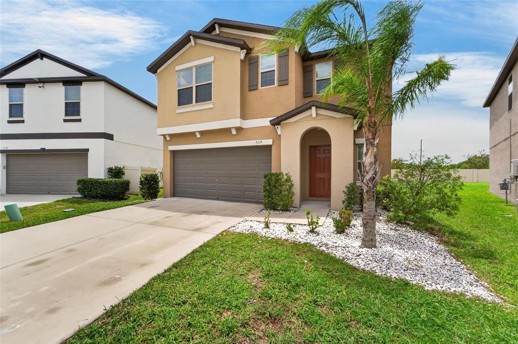 A two-story tan house with a two-car garage and a small palm tree in front — 5119 WHITE CHICORY DRIVE, APOLLO BEACH, FL