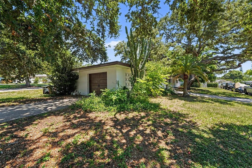 A white detached garage with a brown door sits on a grassy lot with trees — 217 GARDEN CIRCLE, BELLEAIR, FL