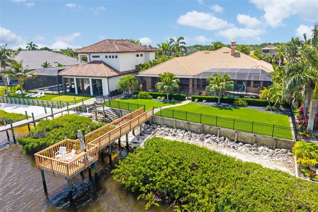 An aerial view shows two waterfront houses with pools, a green lawn, and a wooden dock — 4015 HAWK ISLAND DRIVE, BRADENTON, FL