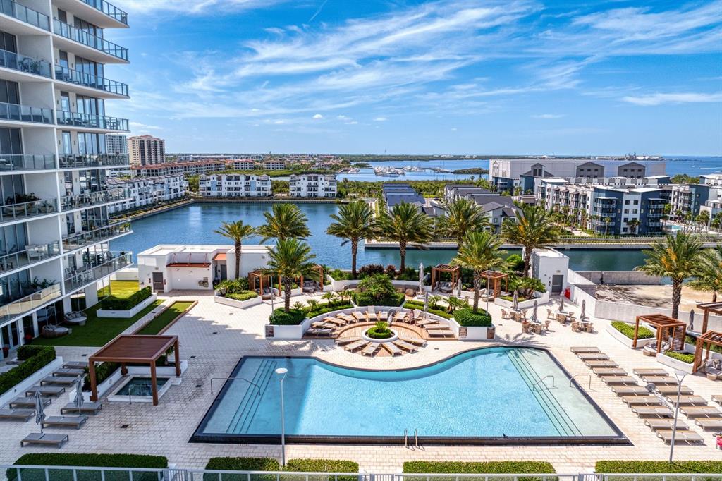 An elevated view of a swimming pool deck with lounge chairs, palm trees, and water — 5120 MARINA WAY UNIT 10006, TAMPA, FL