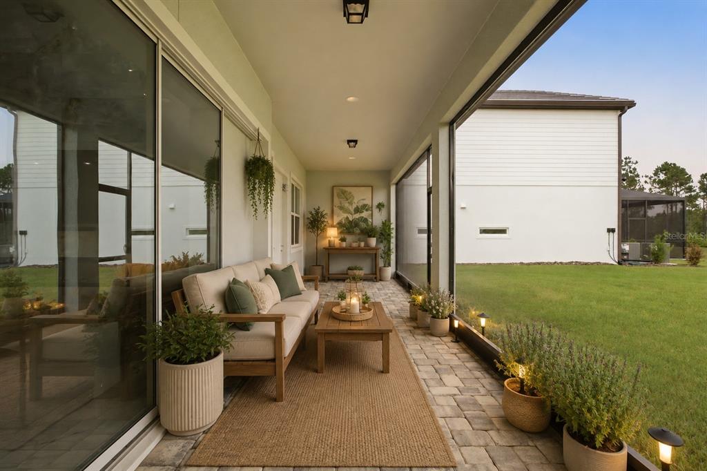 A covered patio with a sofa, coffee table, and potted plants overlooks a grassy backyard — 1515 VALIER POINT, ZEPHYRHILLS, FL