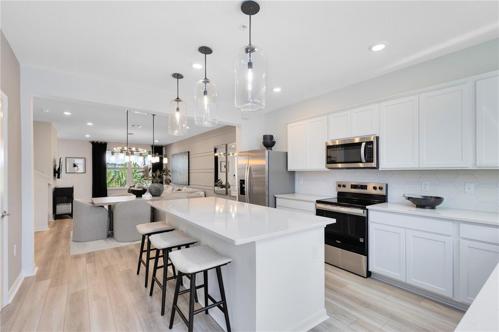 A modern kitchen features white cabinetry, a central island with bar stools, and stainless appliances — 15512 PEACEFUL PINES ALLEY, CLERMONT, FL