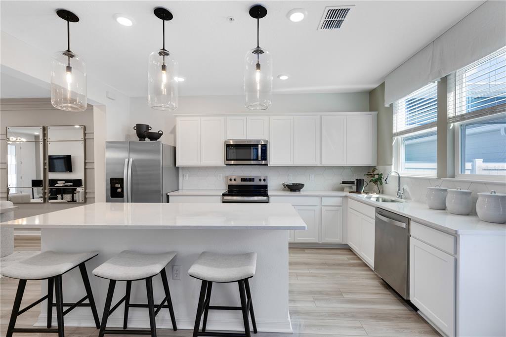 A modern kitchen features white cabinets, stainless steel appliances, a quartz island, and three barstools — 15512 PEACEFUL PINES ALLEY, CLERMONT, FL
