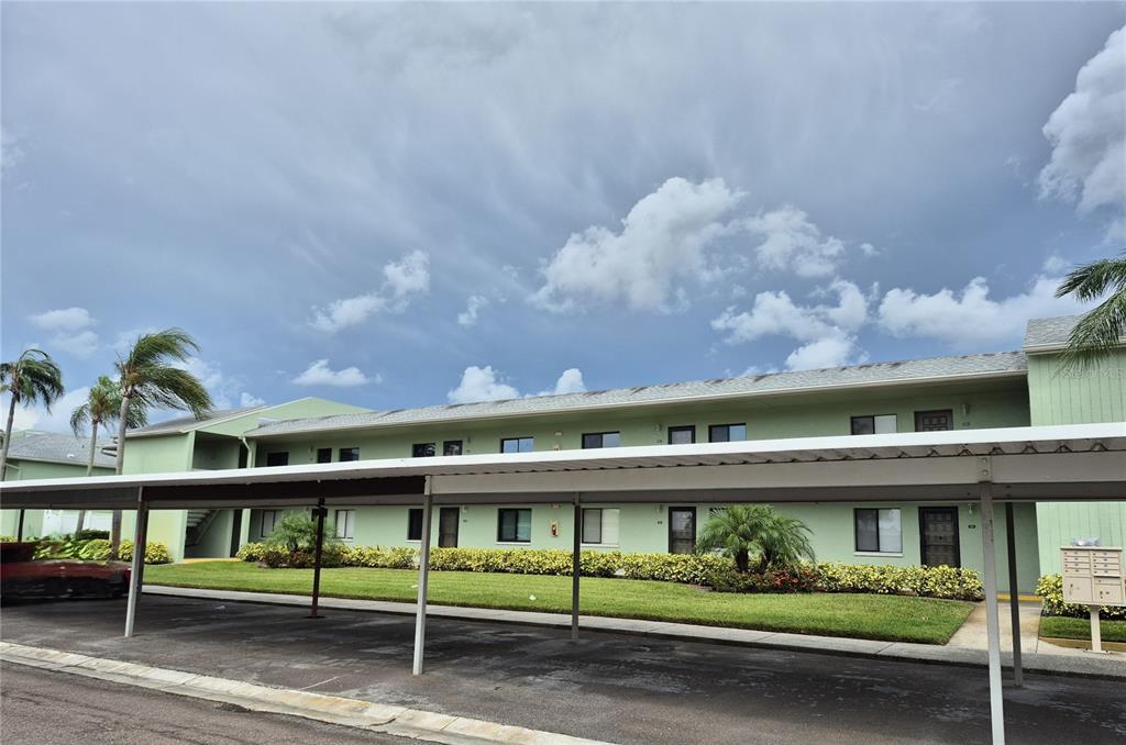 A two-story light green apartment building features a covered parking area in the foreground — 222 CARYL WAY, OLDSMAR, FL