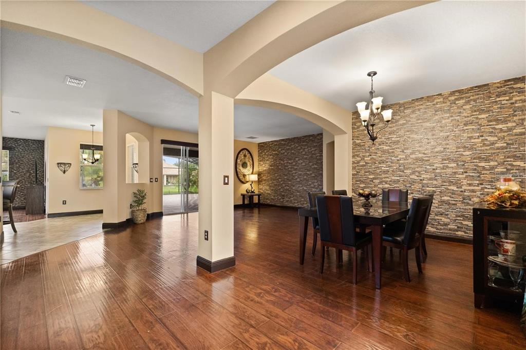 A dining area with a stone accent wall and dark wood flooring under arched ceilings — 3759 EAGLE ISLE CIRCLE, KISSIMMEE, FL