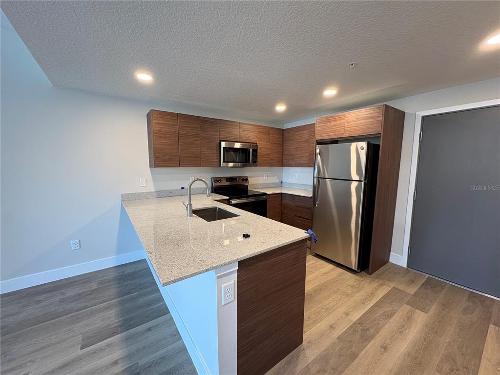 A modern kitchen features wood-grain cabinets, stainless steel appliances, and a granite-topped island — 4424 S TEXAS AVENUE UNIT 1-104, ORLANDO, FL