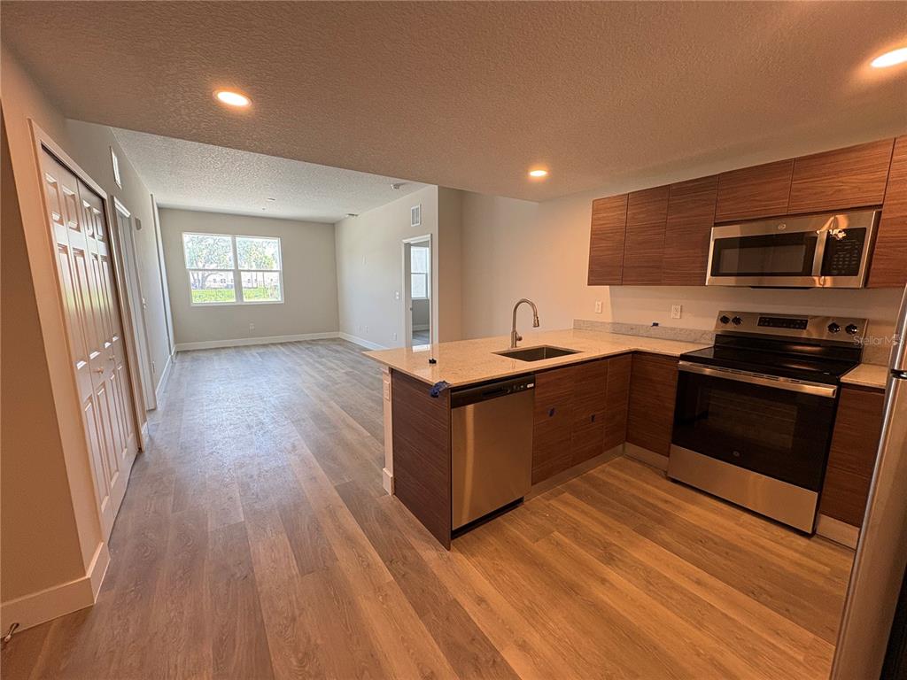 A kitchen with wood-tone cabinets and stainless steel appliances opens into a living area — 4424 S TEXAS AVENUE UNIT 1-104, ORLANDO, FL