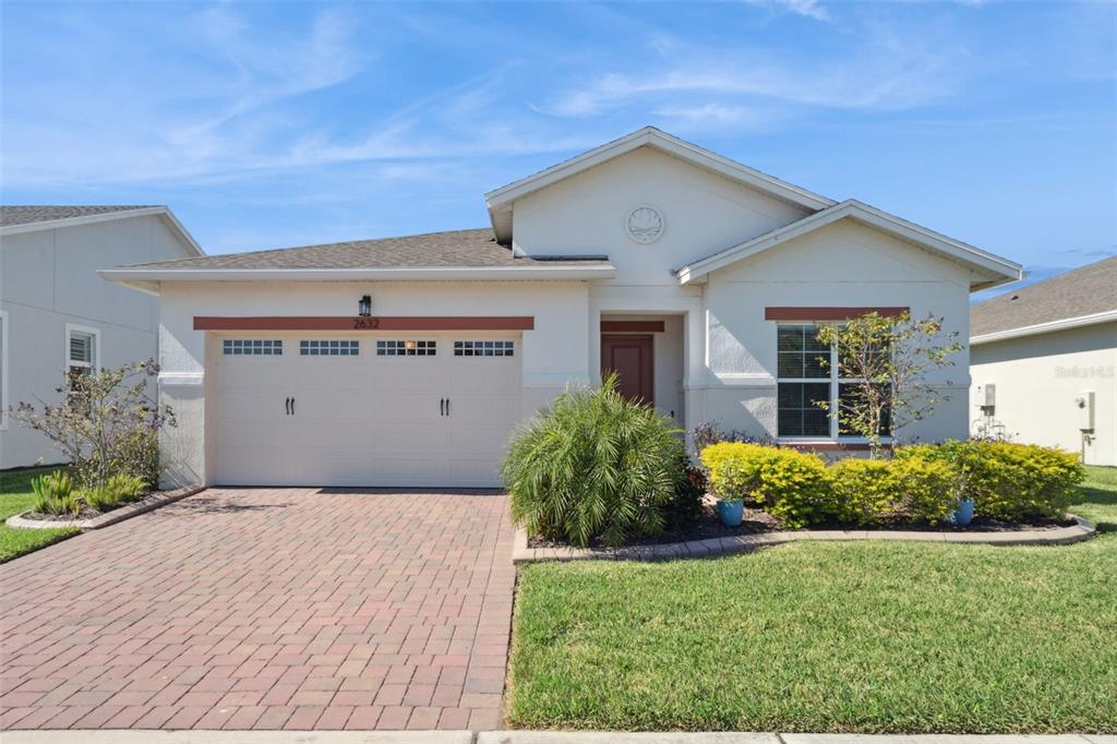 A single-story house with a beige exterior, a two-car garage, and a brick paver driveway — 2632 MEADOWEDGE LOOP, ST CLOUD, FL