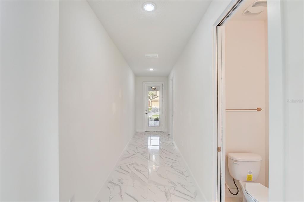 A bright hallway with white marble-look tile flooring leads to an exterior glass door — 3889 WALKER ROAD, APOPKA, FL