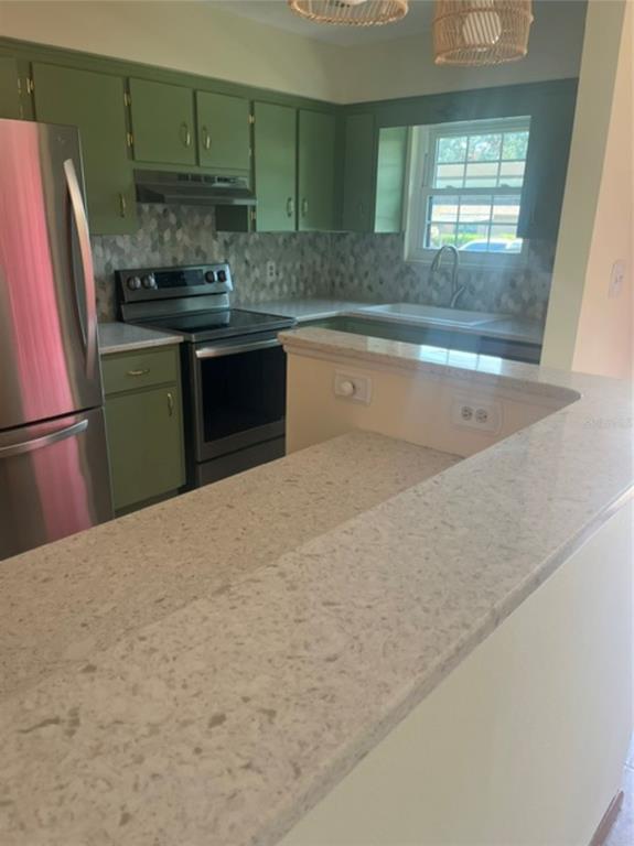 A kitchen features green cabinets, stainless steel appliances, and a light-colored quartz countertop peninsula — 15 COVE LANE, EUSTIS, FL