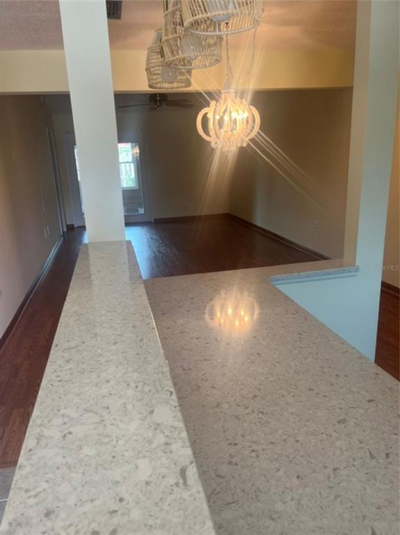 A kitchen counter with light-colored speckled countertops overlooks an open living area with wood flooring — 15 COVE LANE, EUSTIS, FL