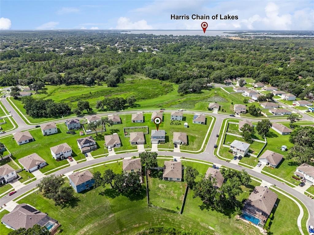 An aerial view shows a suburban neighborhood with houses, green lawns, and a distant lake — 10528 BRONZE LEAF COURT, LEESBURG, FL
