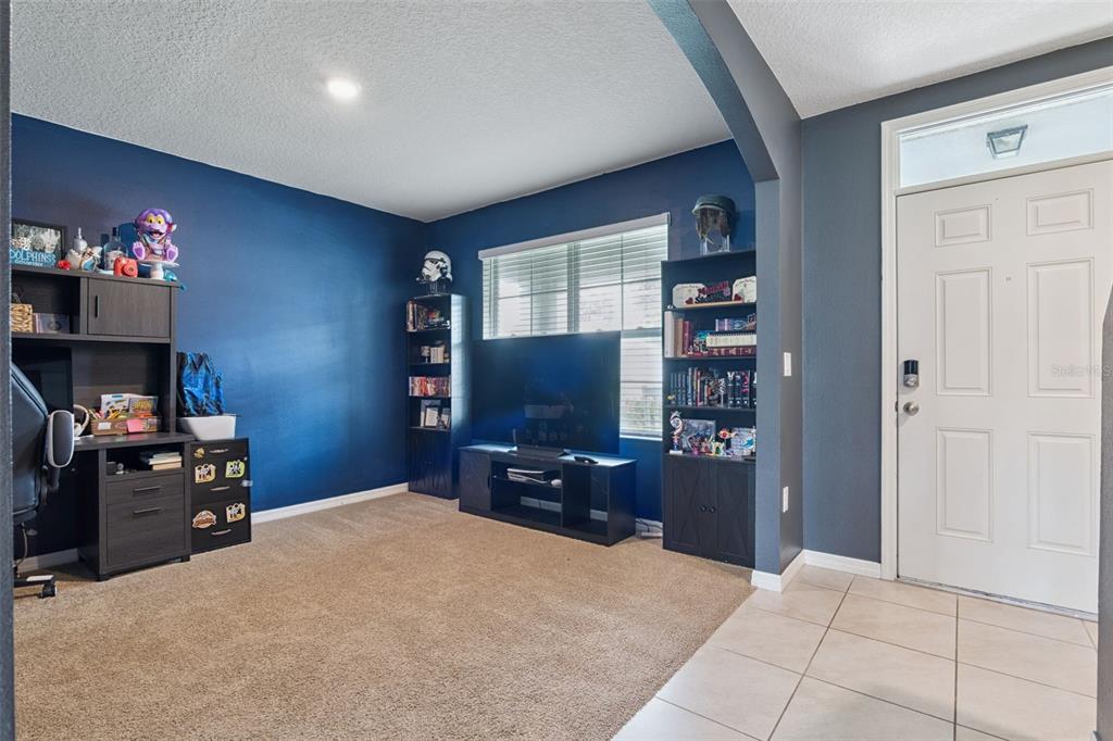 A room with blue walls, carpeted flooring, a desk, a television, and a front door — 10528 BRONZE LEAF COURT, LEESBURG, FL