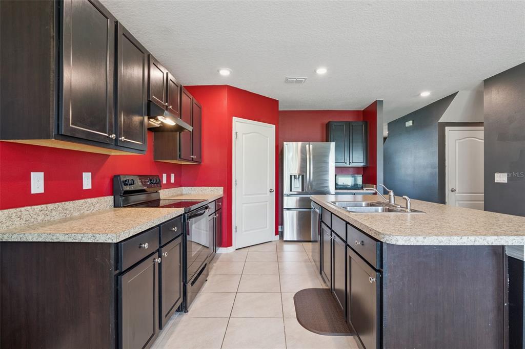 A kitchen features dark wood cabinets, red walls, stainless steel appliances, and a granite-topped island — 10528 BRONZE LEAF COURT, LEESBURG, FL