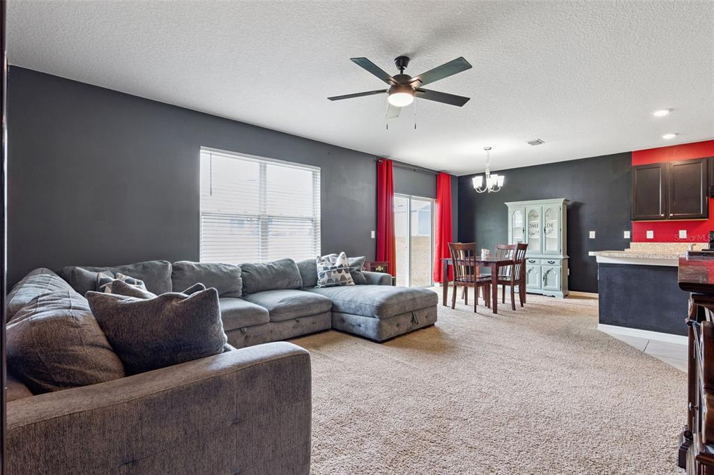 A living room with gray carpet, a sectional sofa, and a dining area with dark walls — 10528 BRONZE LEAF COURT, LEESBURG, FL