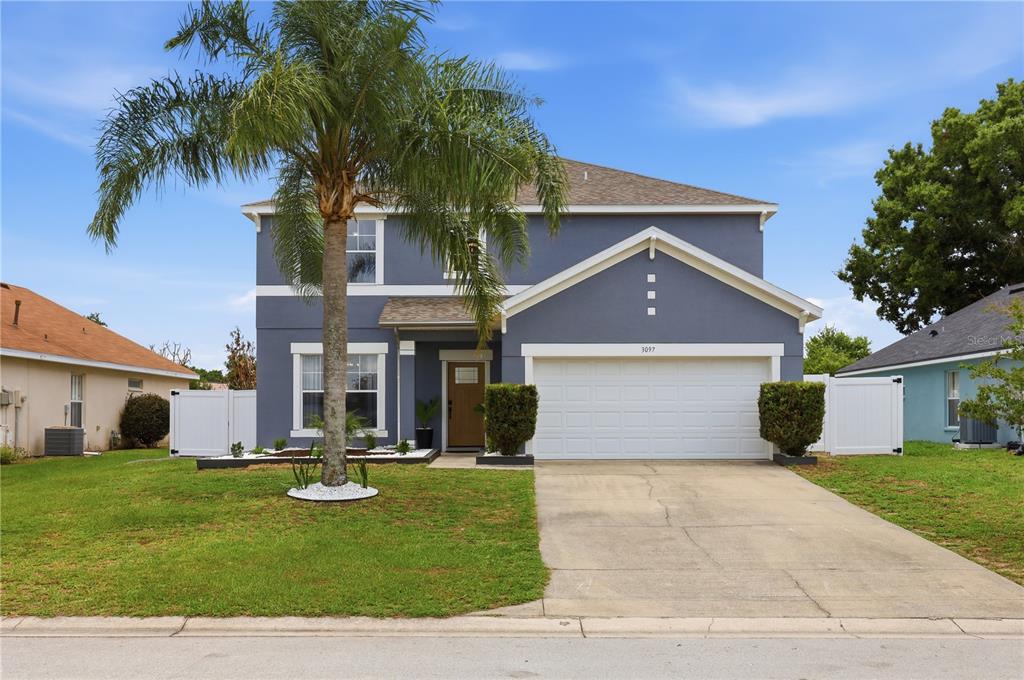 A two-story house with blue stucco siding, a white garage door, and a palm tree — 3097 BUCKEYE POINTE DRIVE, WINTER HAVEN, FL