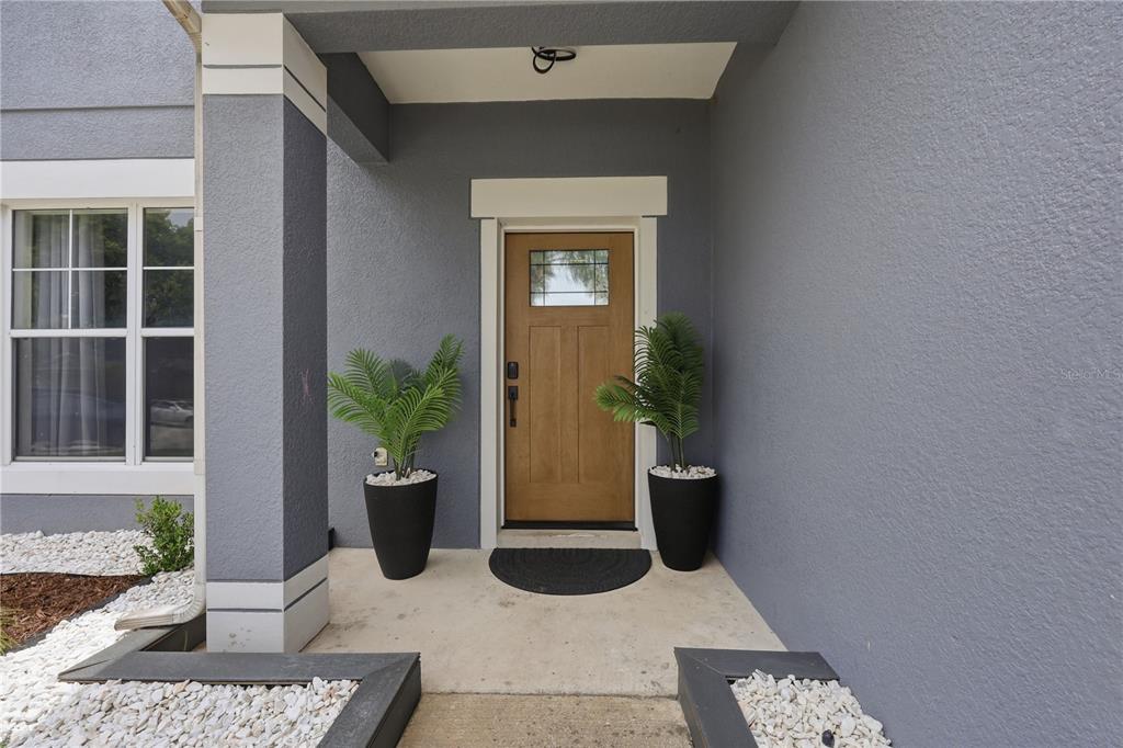 A front entryway features a wooden door, two potted plants, and gray stucco walls — 3097 BUCKEYE POINTE DRIVE, WINTER HAVEN, FL