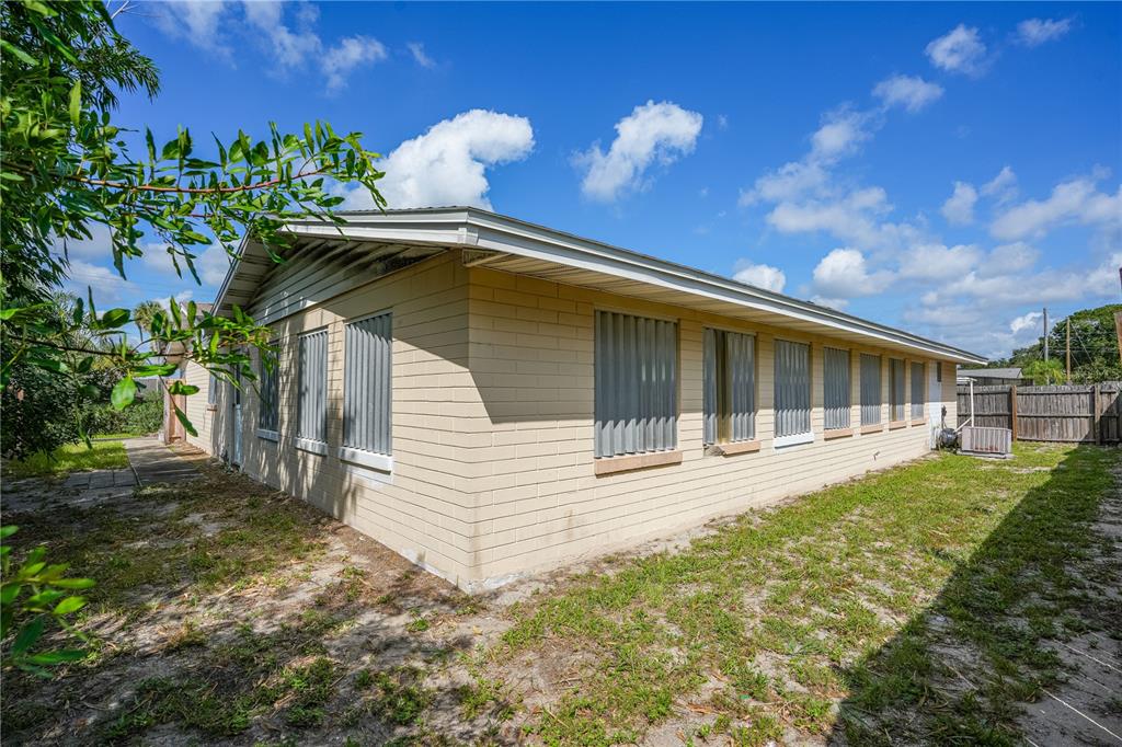 The exterior side of a tan concrete block house features metal hurricane shutters on windows — 2005 SAXON DRIVE, NEW SMYRNA BEACH, FL