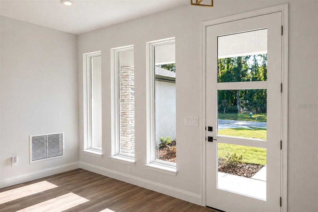 A bright room features light wood-look flooring, white walls, three tall windows, and a glass-paneled door — 14 RENSHAW DRIVE, PALM COAST, FL