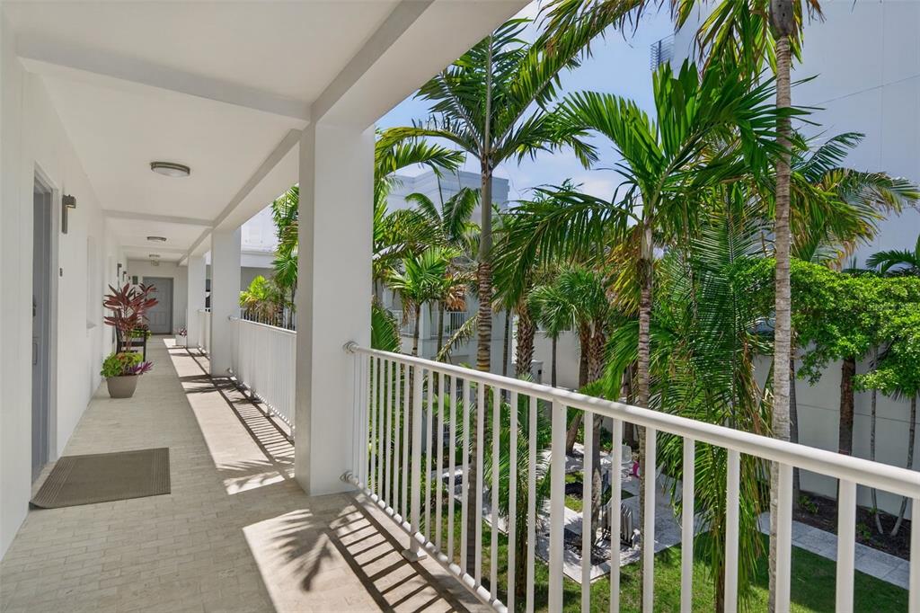 An outdoor apartment walkway features white railings, tiled flooring, and views of tropical palm trees — 433 CENTRAL AVENUE, SARASOTA, FL