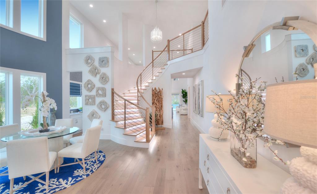 A bright foyer features a curved staircase with illuminated steps, light wood floors, and dining area — 85 CORONADO ROAD, FLAGLER BEACH, FL
