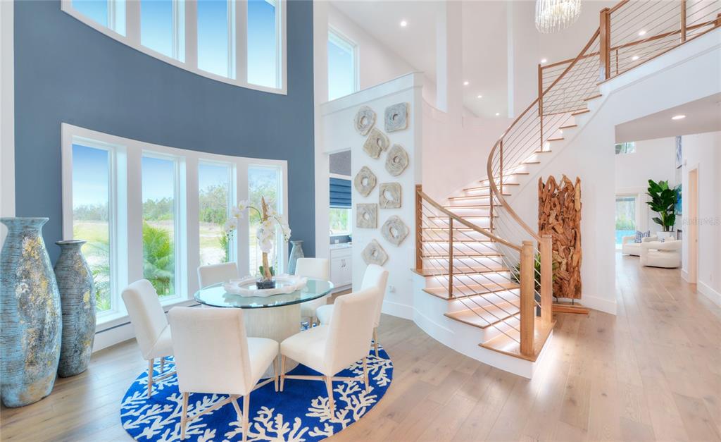 A dining area with a curved staircase, blue accent wall, and large windows — 85 CORONADO ROAD, FLAGLER BEACH, FL