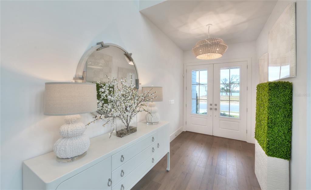 A bright entryway features a white console table, a large round mirror, and double glass doors — 85 CORONADO ROAD, FLAGLER BEACH, FL