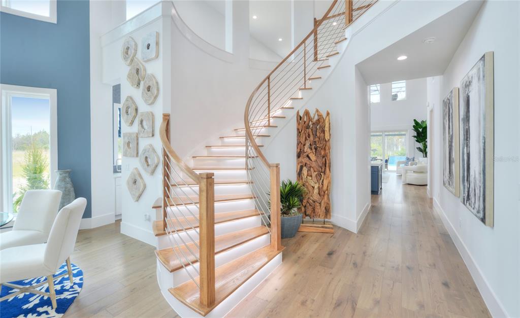 A curved staircase with illuminated wooden treads and metal railings sits in a bright foyer — 85 CORONADO ROAD, FLAGLER BEACH, FL