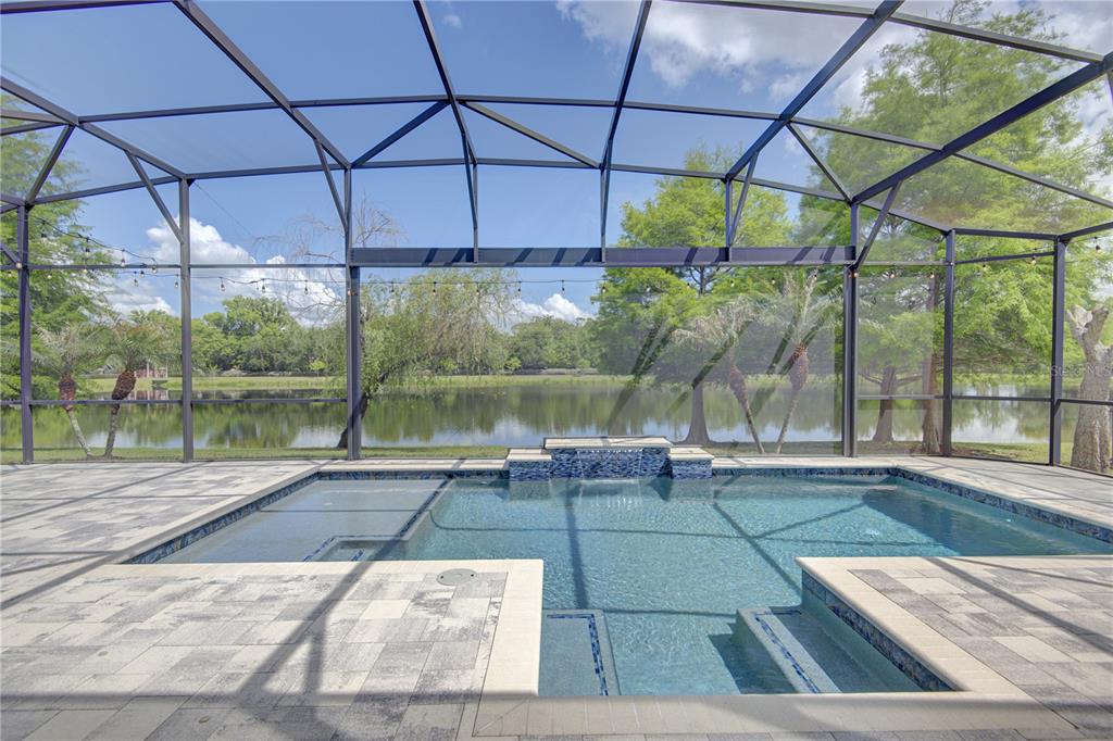 A screened-in pool patio features a rectangular pool with a water feature and paver decking — 1185 STELLAR DRIVE, OVIEDO, FL