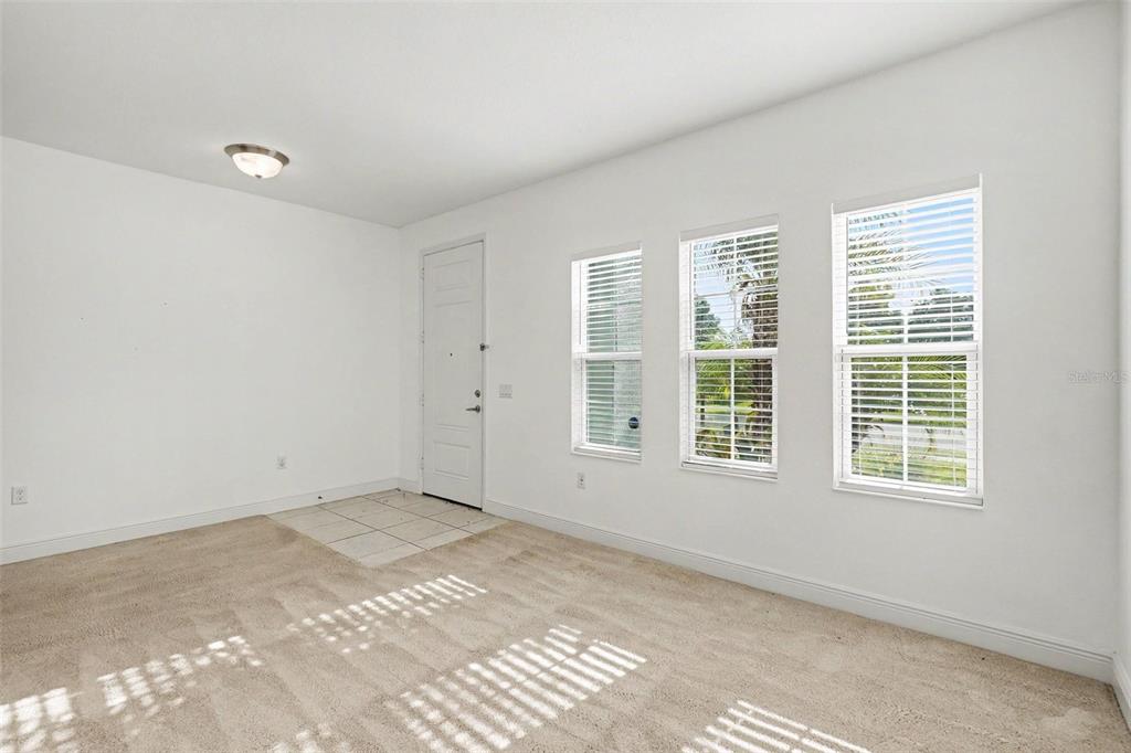 An empty room with beige carpet, a tiled entryway, a white door, and three windows — 4107 PINE MEADOW DRIVE, PARRISH, FL