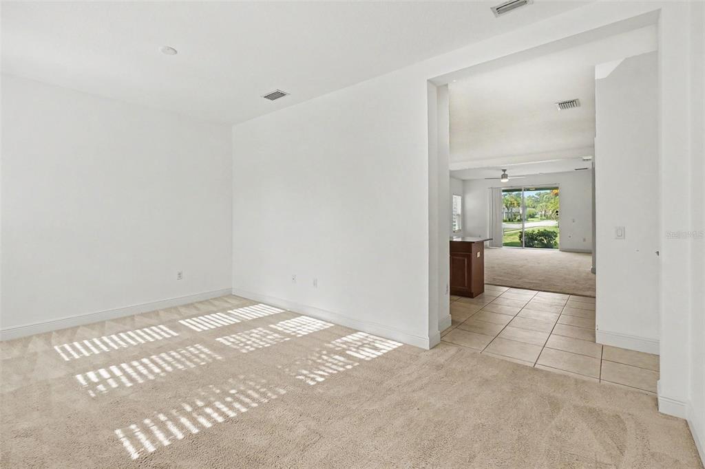 A carpeted room with white walls opens into a tiled kitchen area with sliding glass doors — 4107 PINE MEADOW DRIVE, PARRISH, FL