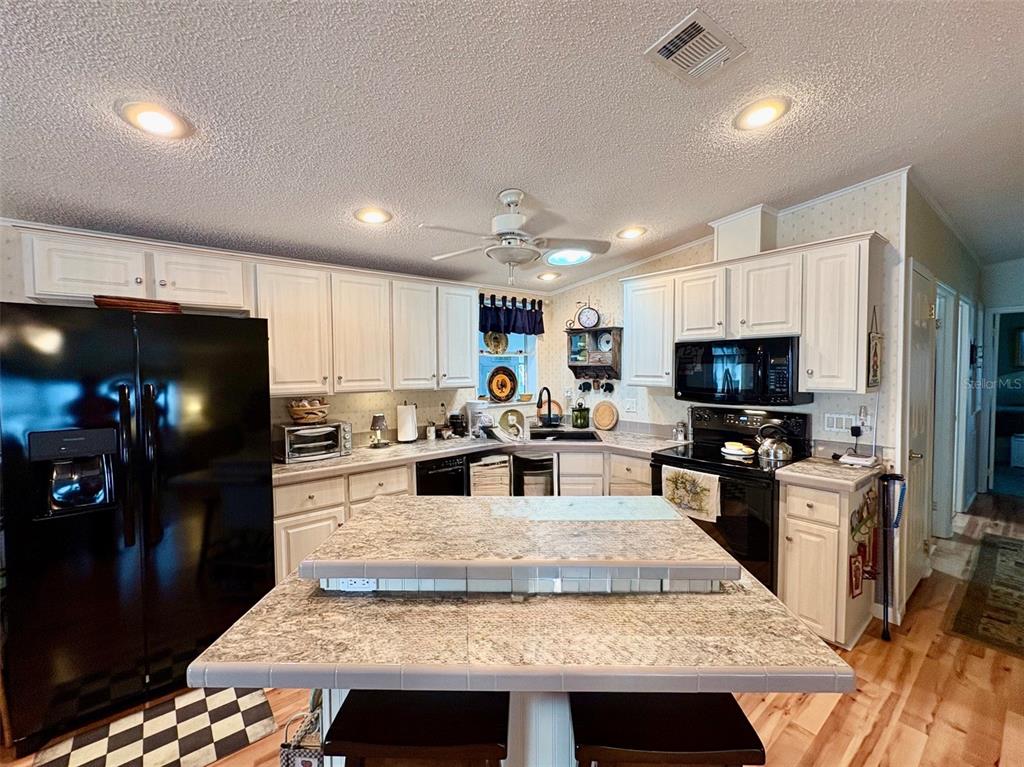 A kitchen features white cabinets, black appliances, a central island, and light-colored countertops — 6600 SCENIC POINT DRIVE SE, WINTER HAVEN, FL