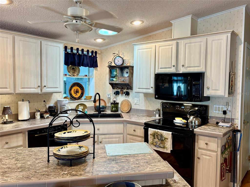 A kitchen sink area features a black faucet, patterned wallpaper, and a wooden wall shelf — 6600 SCENIC POINT DRIVE SE, WINTER HAVEN, FL