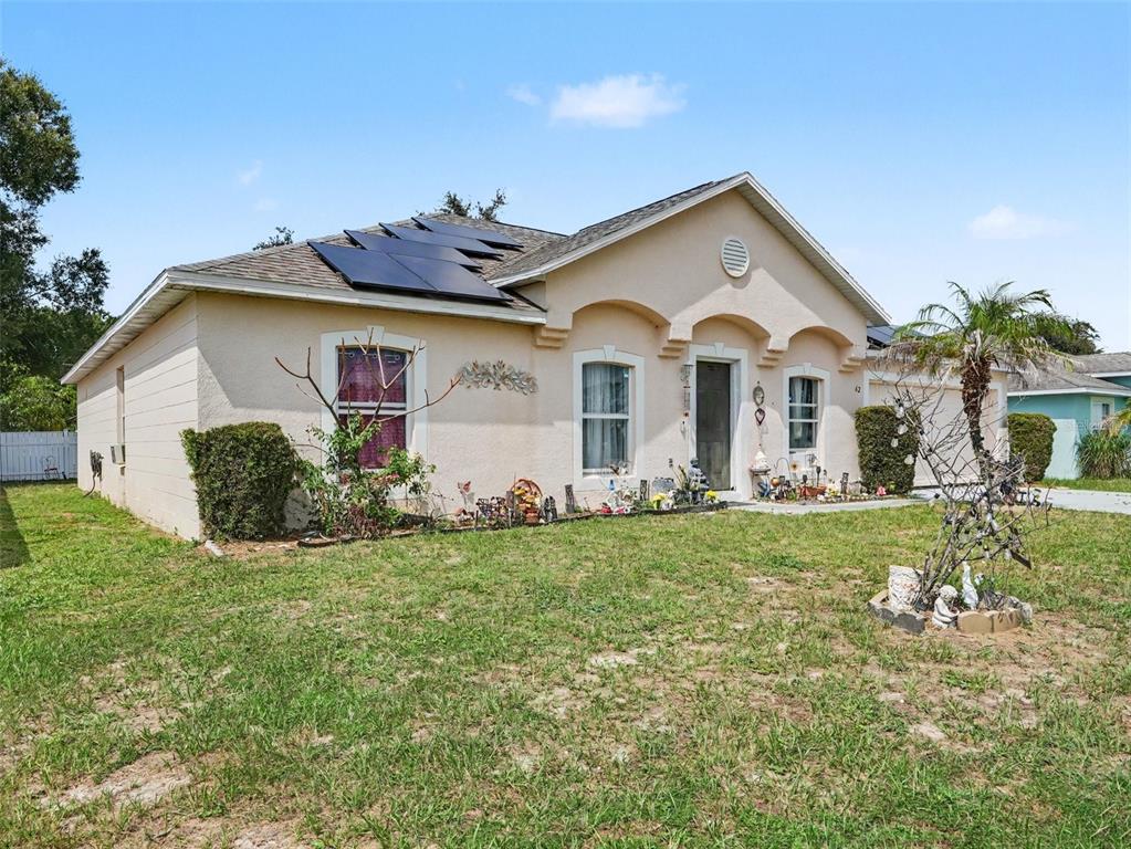 A single-story stucco house with a shingled roof, solar panels, and a front lawn — 62 HERRING COURT, POINCIANA, FL