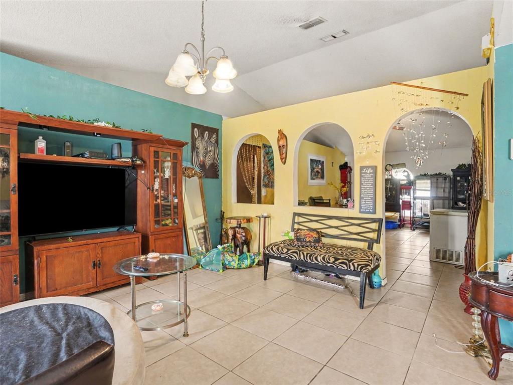 A living room with tile flooring, a large wooden entertainment center, and arched wall openings — 62 HERRING COURT, POINCIANA, FL
