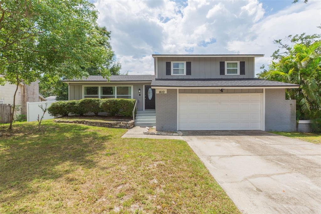 A two-story house with gray siding, a white garage door, and a landscaped front yard — 1610 BURNING TREE LANE, BRANDON, FL