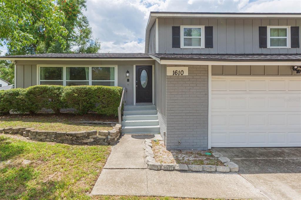 A gray two-story house features a white garage door, a front door with stairs, and landscaping — 1610 BURNING TREE LANE, BRANDON, FL
