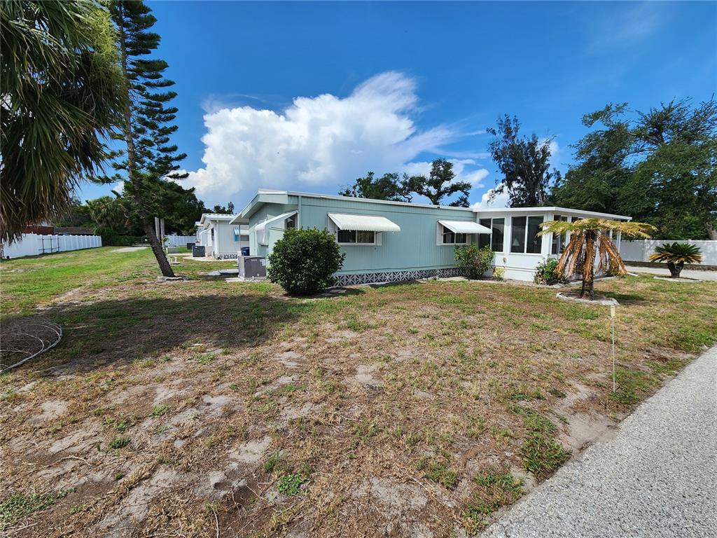 A light blue mobile home with a white sunroom sits on a grassy lot — 808 53RD AVENUE E UNIT 223, BRADENTON, FL