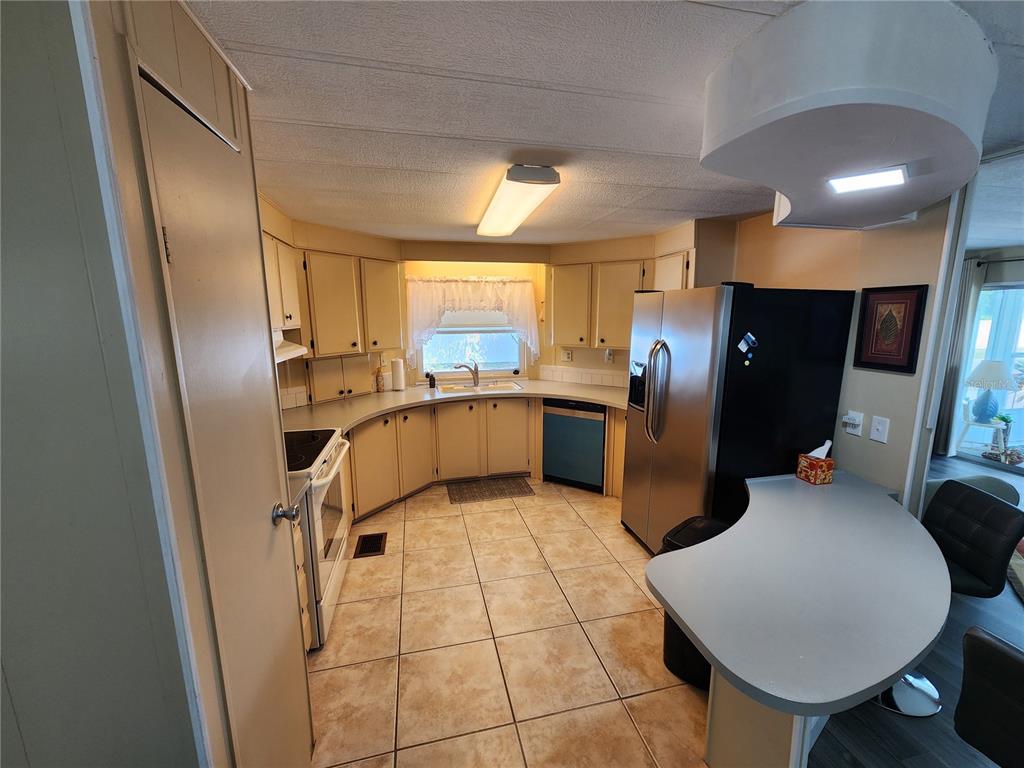 A kitchen features beige cabinets, tile flooring, stainless steel appliances, and a curved breakfast bar — 808 53RD AVENUE E UNIT 223, BRADENTON, FL