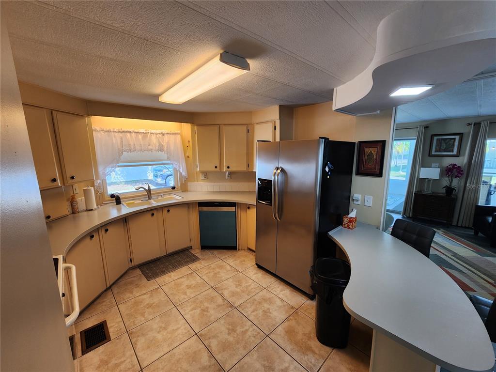 A kitchen with tan cabinets, stainless steel refrigerator, tile flooring, and a curved breakfast bar — 808 53RD AVENUE E UNIT 223, BRADENTON, FL