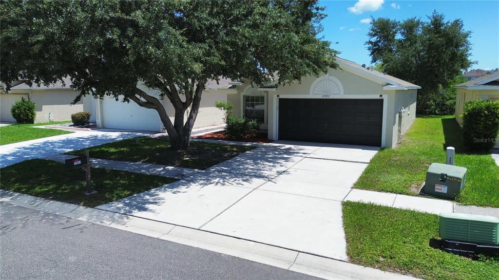 A single-story house with a dark garage door, a large tree, and a concrete driveway — 12922 FIELDMOOR COURT, RIVERVIEW, FL