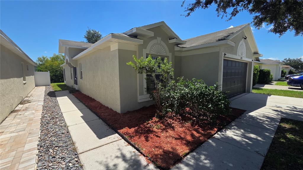 The exterior of a single-story house features a garage, a paved walkway, and landscaping — 12922 FIELDMOOR COURT, RIVERVIEW, FL
