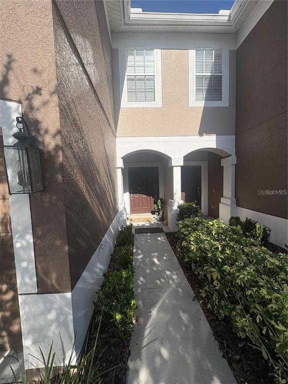 A concrete walkway leads to the brown front door of a two-story stucco townhouse — 4605 BARNSTEAD DRIVE, RIVERVIEW, FL