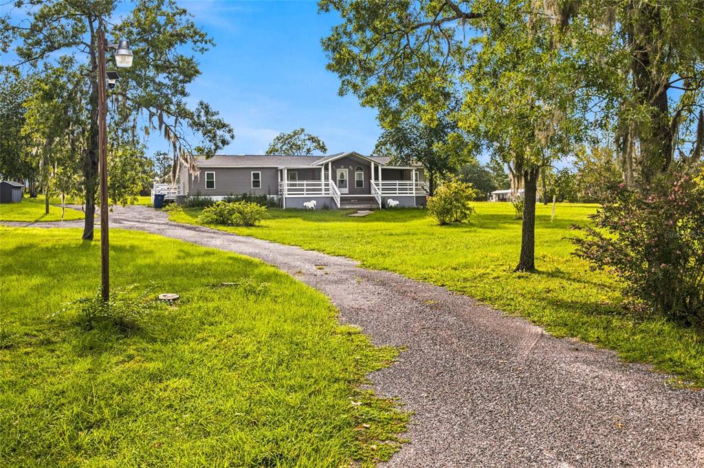 A gravel driveway leads to a gray manufactured home with a white porch and railing — 5351 NE 121ST TERRACE, WILLISTON, FL