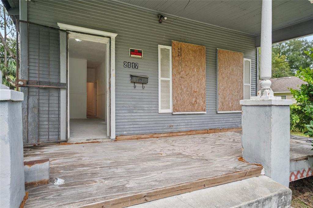 A weathered front porch leads to an open doorway of a house with boarded windows — 2117 TUSKEGEE ROAD, JACKSONVILLE, FL