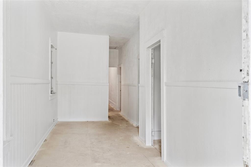 A narrow, white-walled hallway features beadboard wainscoting and an unfinished concrete floor — 2117 TUSKEGEE ROAD, JACKSONVILLE, FL