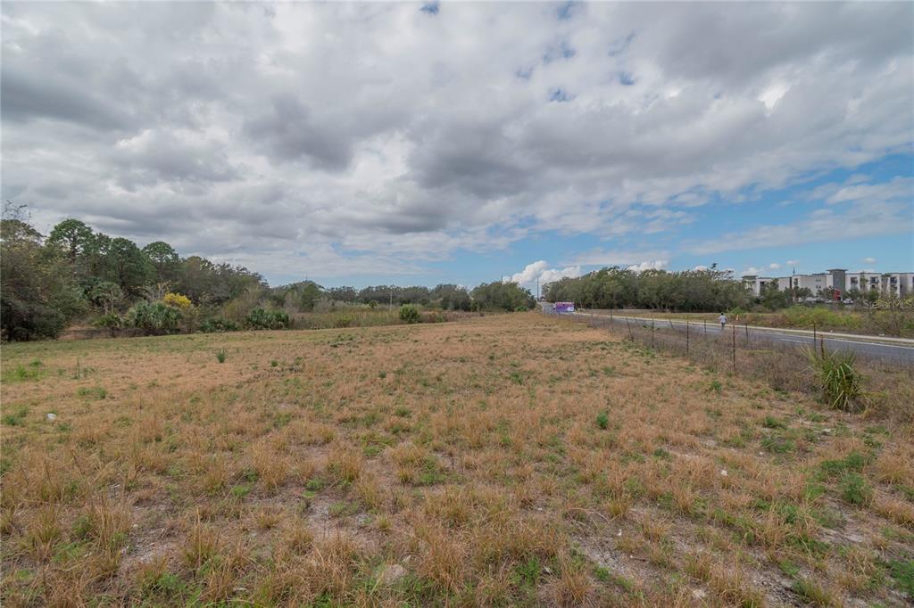 A large, flat, grassy vacant lot sits next to a road with trees in the background — 46 A, SANFORD, FL